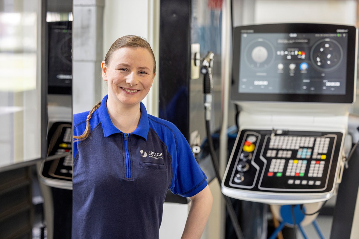 Eine Frau steht neben einer technischen Anlage und lächelt freundlich in die Kamera.