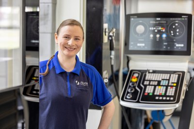 Eine Frau steht neben einem technischen System und lächelt freundlich in die Kamera.