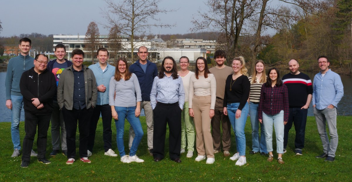 A group of people standing together outdoors on a grassy area with trees and buildings in the background. (Mistral: Pixtral Large 2411, 2026-03-30)